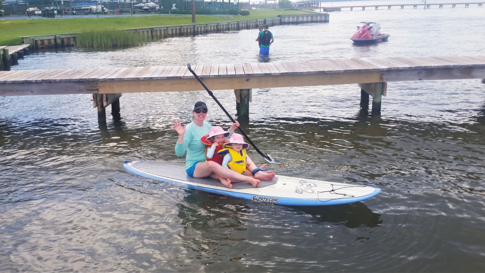 A woman and two children sitting on a paddleboard with a dock behind them.