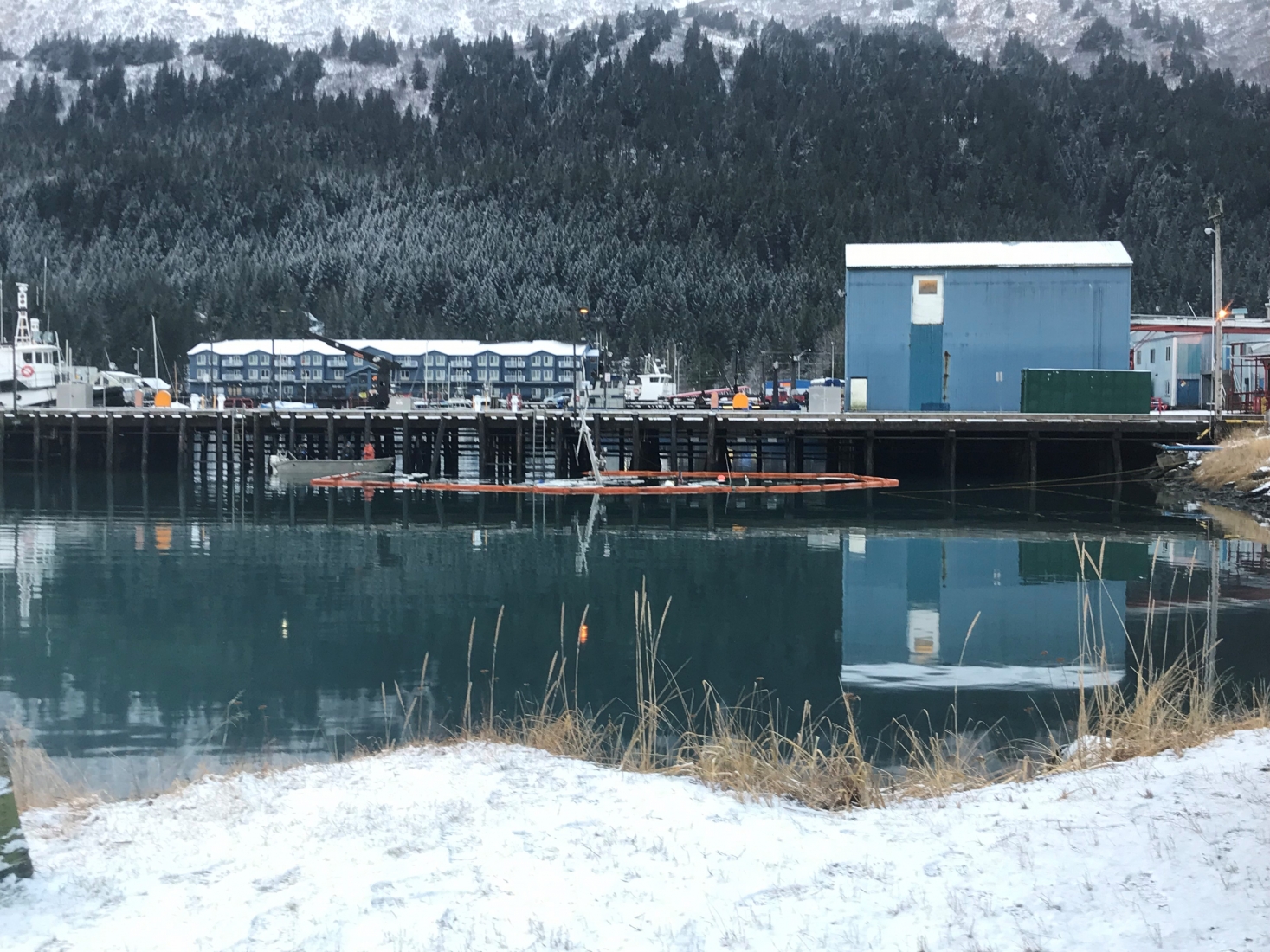 Orange pollution boom around a sunken vessel with snowy mountains in the background.