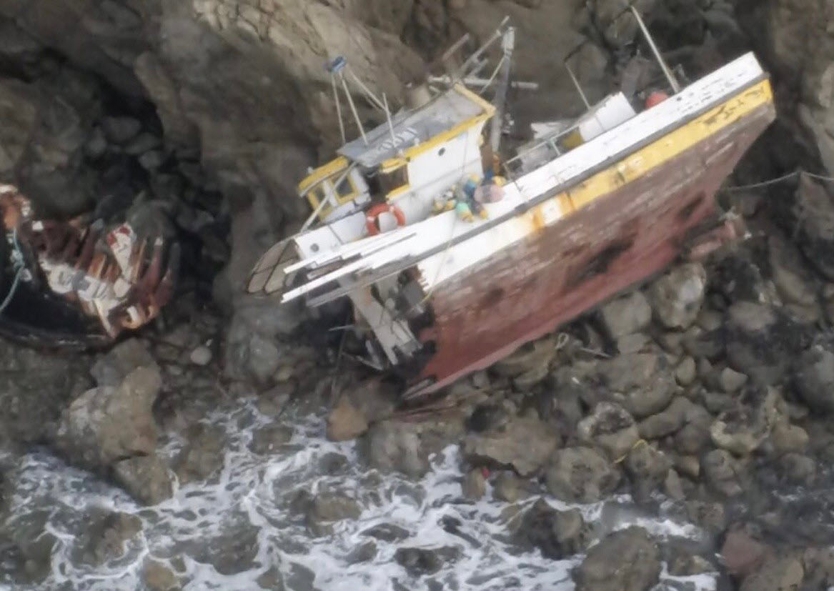 Fishing vessel broken into two pieces after grounding up against a steep, rocky, coastal terrain.