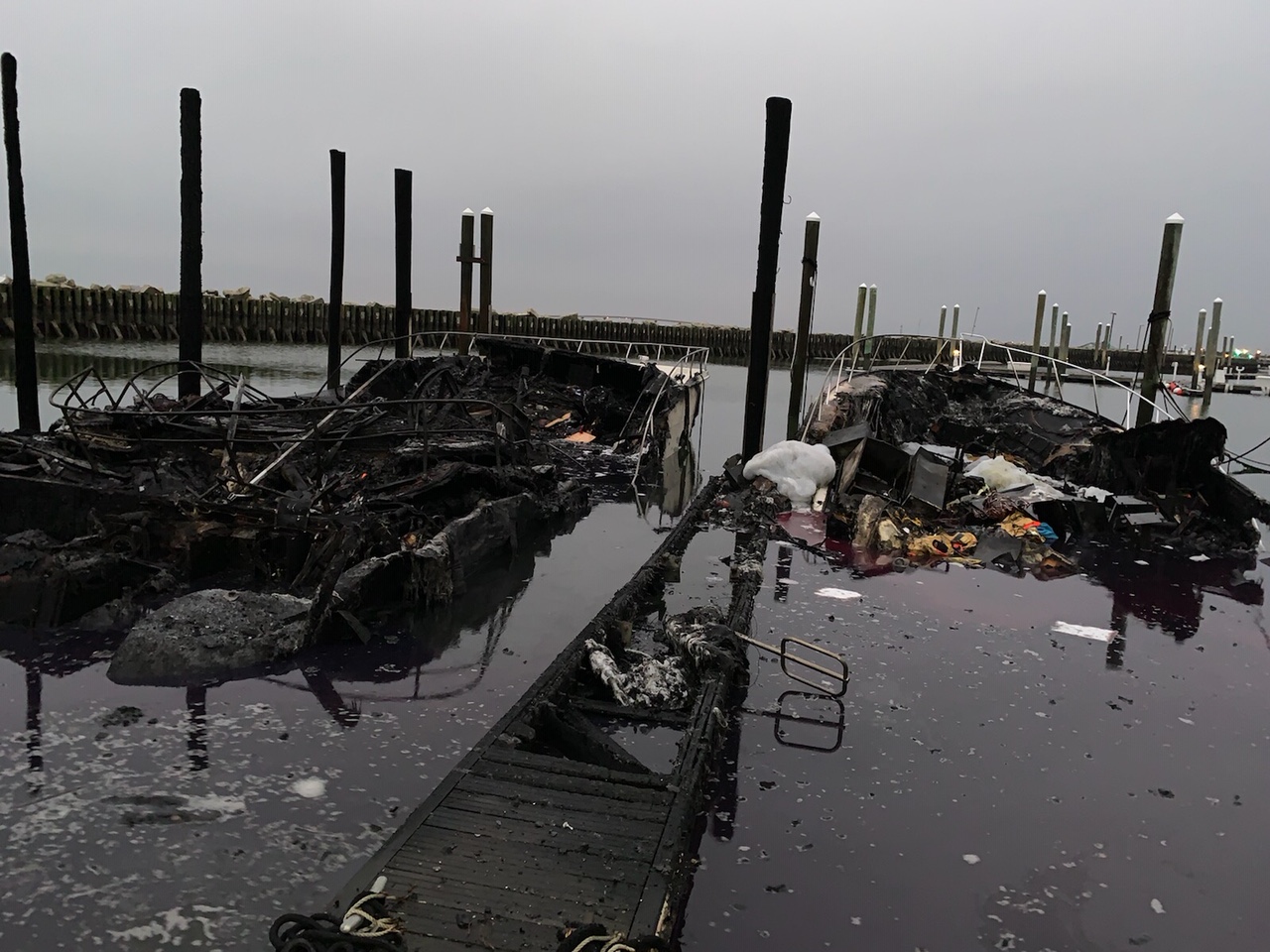 Two burned vessels partially submerged in a marina. 