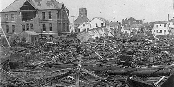 A black and white photo of a street with collapsed and demolished buildings.