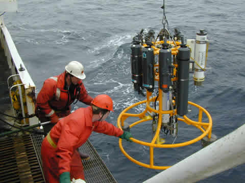 Two men pulling a scientific instrument aboard a vessel. 