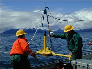 Two people on a vessel lowering an instrument into the water. 