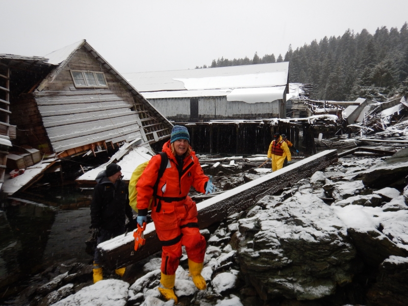 A woman in response gear near a collapsed structure covered in snow.