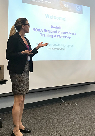 A woman standing in front of a projector screen that reads "Norfolk NOAA Regional Preparedness Workshop and Training." 