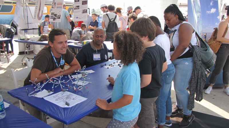 A group of kids at a table with molecule models talking to two NOAA staff.