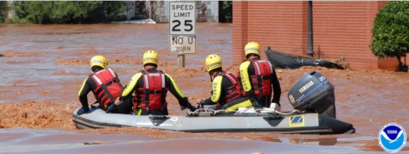 A boat with several people in response gear floating through a flooded street.