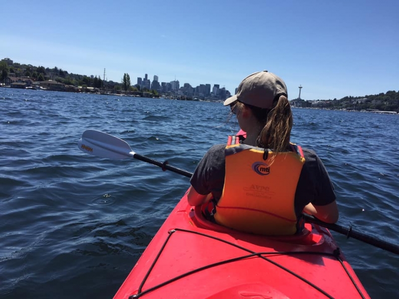 A girl in a kayak with a city skyline in the background.