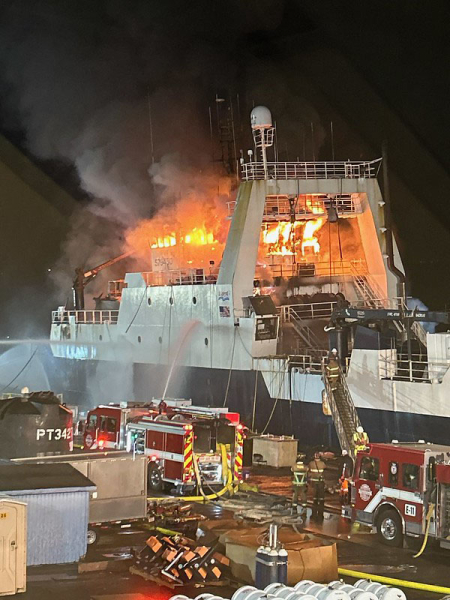 Fire Department vehicles alongside a ship on fire.