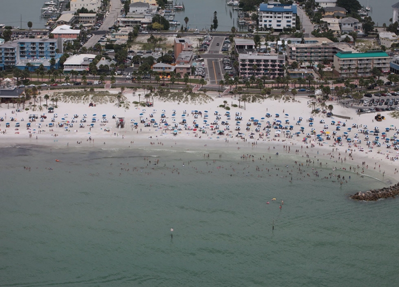 An aerial view of a beach with people on it and a city in the background. 