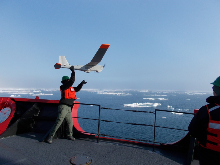 A man launching an unmanned aerial vehicle, or drone, from the bow of a vessel. 