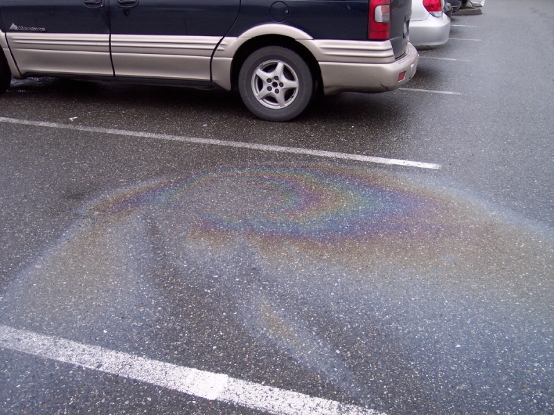 A parking lot with a rainbow-colored sheen in a puddle. 