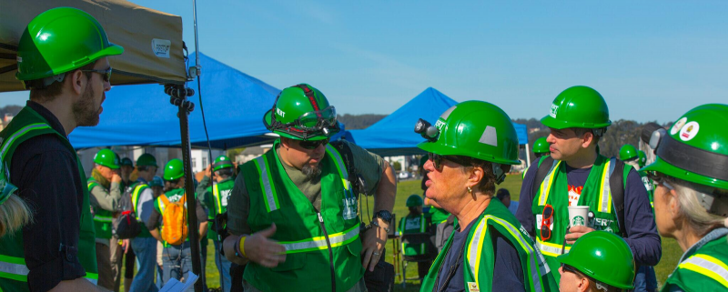 A group of people in green hard hats and reflective vests.