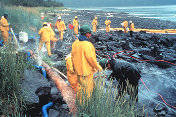 Workers in yellow doing cleanup operations on a rocky shoreline.