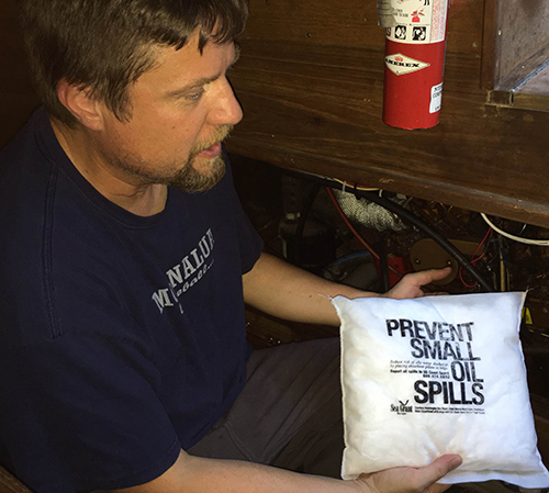 A man holding up an absorbent oil spill prevention kit pillow that reads, "Prevent small oil spills." 