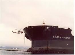 A black and white photo of a helicopter approaching with a vessel with the name "Exxon Valdez" on it. 