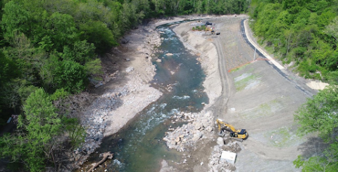 An aerial view of a construction vehicle working alongside a river. 
