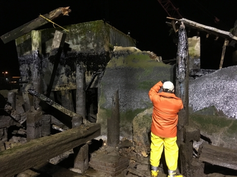A man in response gear inspects an oiled pier. 