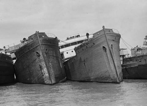 A black and white photo of two wooden ships tied together. 
