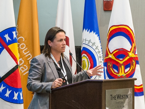 A woman talking at a podium with several flags behind her. 