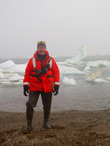 A man standing on a rocky beach with sea ice in the background.