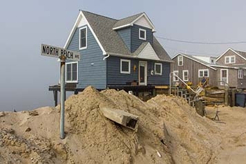 A house raised above a sandy shoreline with debris in it. 