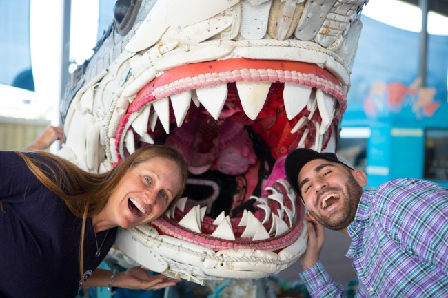 Two people stick their heads into a shark sculpture.