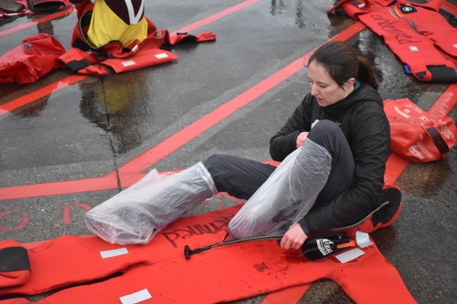 A woman with plastic bags on her feet reaches her feet into a survival suit.