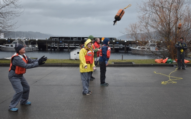 A woman in a life preserver reaches out her arms to catch a flying object.