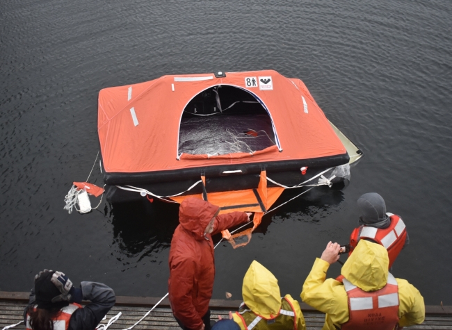 A group of people in response gear standing on a dock looking at a life raft. 