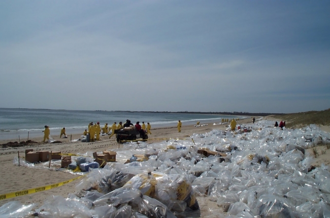 A beach covered in plastic bags filled with oil-soiled materials and cleanup workers in yellow protection gear.