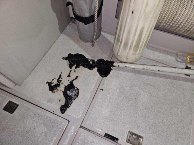 A sample of a sticky, black, tar-like substance obtained by on-scene responders is present on the floor of a vessel