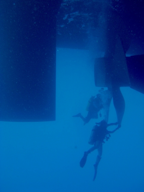 An underwater image of two underwater divers near a ship's propellers. 