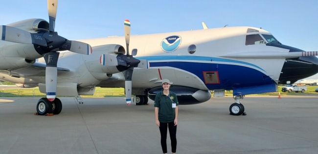 A girl standing in front of a plane with a NOAA logo on it.