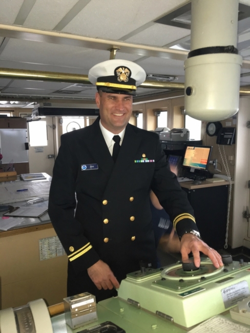 A man in a ship captain's uniform in the control room of a ship. 