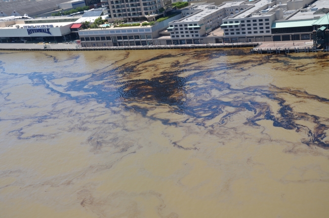 An aerial view of oil in water along an urban shoreline.