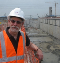 A man in a hard hat and orange vest with an empty canal behind him.