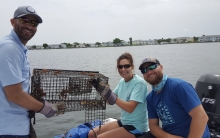 Three people holding up a crabbing cage.