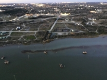 An aerial view of dark crude oil in a body of water along an urban shoreline.