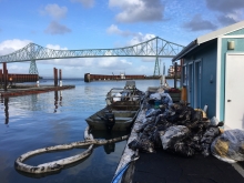 A boat next to a dock with garbage bags filled with oiled debris on it. A bridge is in the background