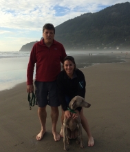 A man, a woman, and a dog posing on a beach for a photo. 