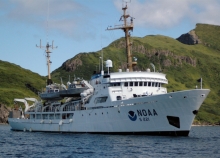 A vessel with a NOAA logo in a body of water with mountains in the background. 