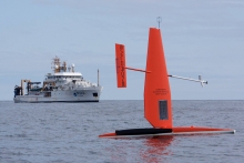 A saildrone in the water with a vessel in the background. 
