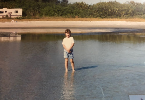 A young person stands in a shallow pool of water smiling for a picture.
