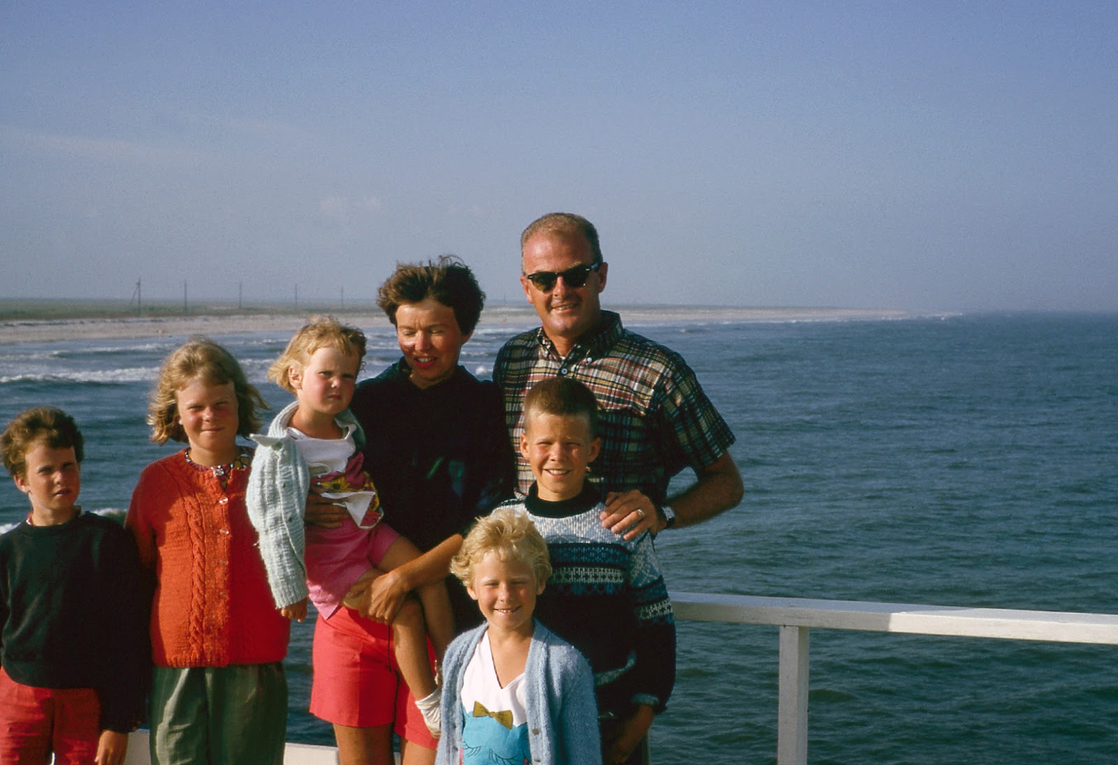 A family of seven posing for a photo in front of a body of water.