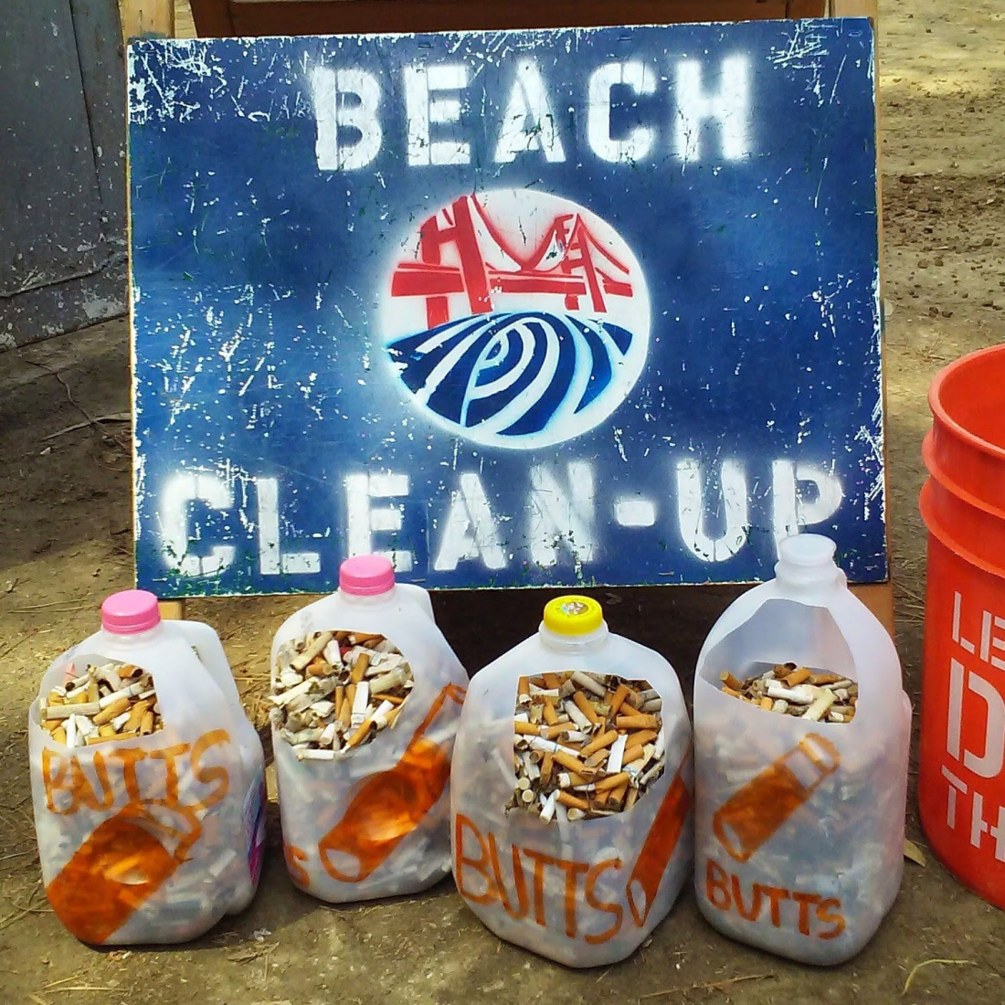 Milk jugs holding collected cigarette butts next to a beach cleanup sign.
