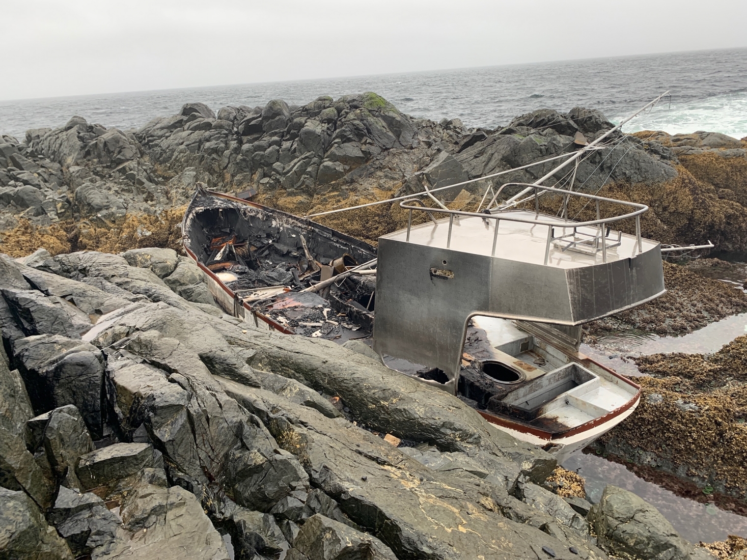 A vessel with visible fire damage grounded on a rocky shore. 