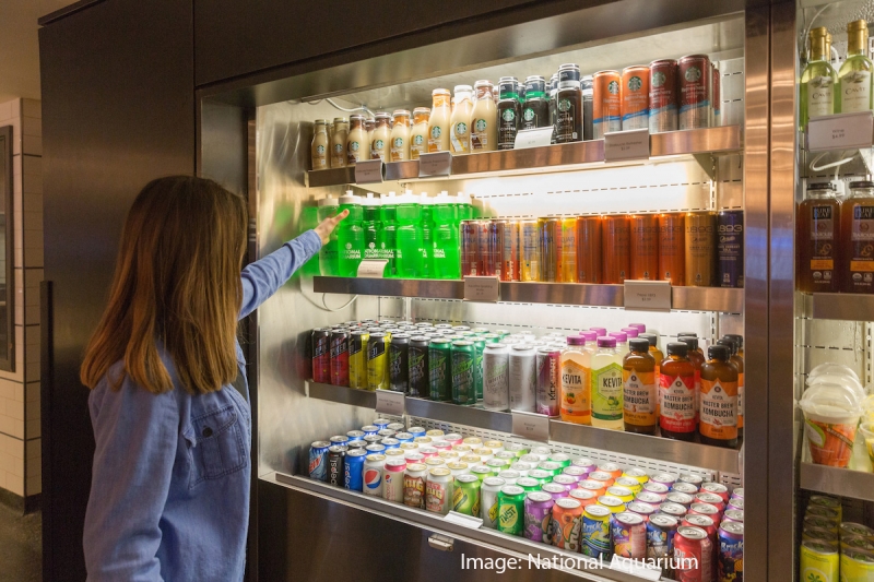 A woman reaches into a beverage case for a water bottle. 