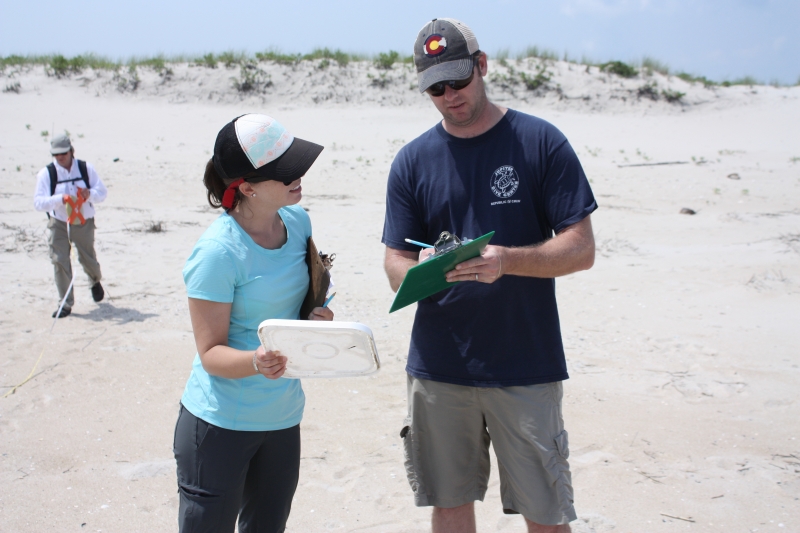 Two people on a beach looking at clipboards. 