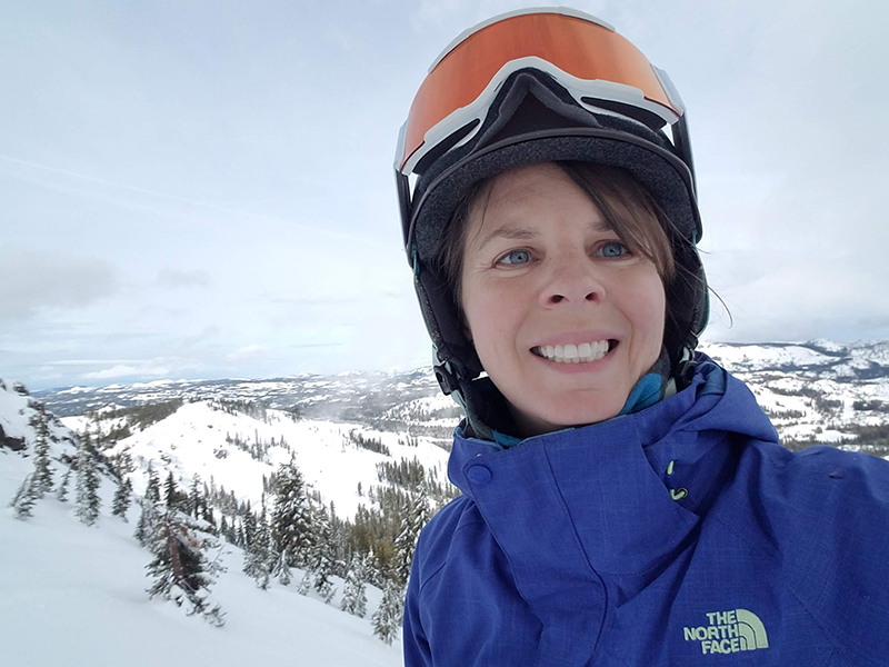A woman in ski gear with a snowy mountain in the background.